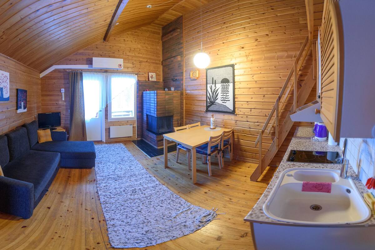 Acogedor interior de una cabaña de madera con sala de estar, una mesa de comedor y cocina.