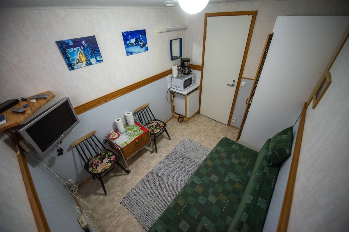 Una habitación pequeña y funcional con cama, escritorio con computadora, silla, microondas y dos cuadros en la pared.