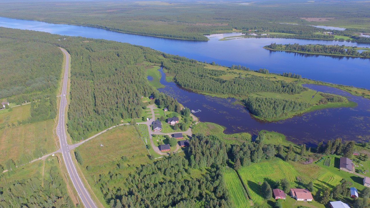 Vue aérienne d’une propriété au bord d’un lac, avec une route, des maisons et une forêt dense.