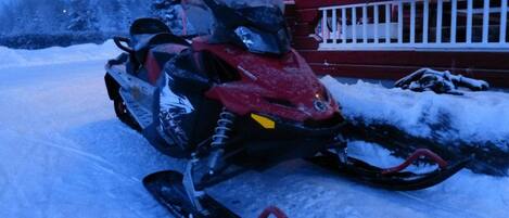 Ein Schneemobil steht auf einer mit Schnee bedeckten Fläche, im Hintergrund eine rote und weiße Struktur.