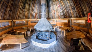 A traditional igloo interior with a central fire pit, wooden benches, and fur rugs. - Holiday Village Kuukiuru (Kemijarvi)