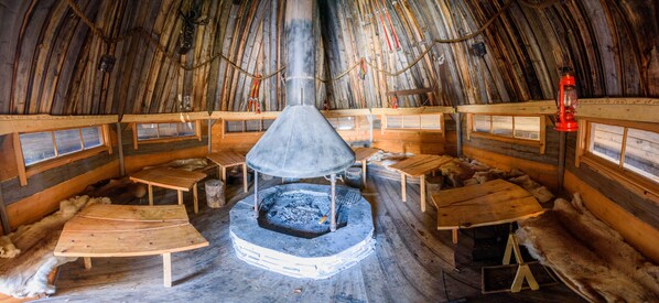 A traditional igloo interior with a central fire pit, wooden benches, and fur rugs. - Holiday Village Kuukiuru (Kemijarvi)