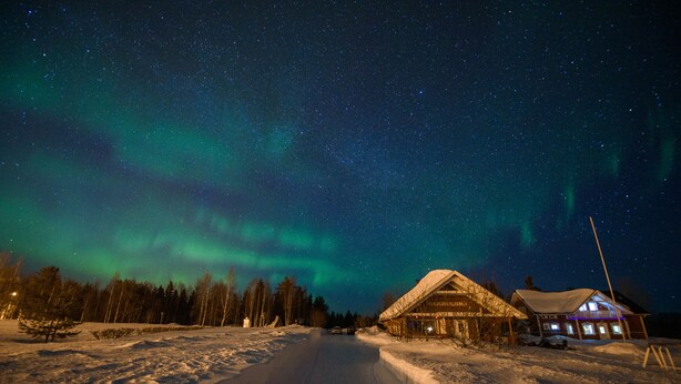 A snow-covered road leading to a wooden cabin with a snow-covered roof and a lit signboard. - Holiday Village Kuukiuru (Kemijarvi)