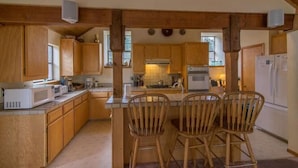 A kitchen with wooden cabinets, a microwave, a stove, and a refrigerator. There are two wooden chairs at a small table.