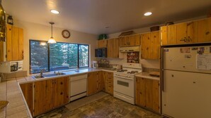 A kitchen with wooden cabinets, a stove, a refrigerator, and a window with a view of trees. - Gamara 3 Bedroom Holiday Home By Tahoe Truckee (Truckee)