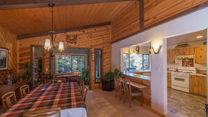 A wooden cabin interior with a dining area, kitchen, and large windows. - Gamara 3 Bedroom Holiday Home By Tahoe Truckee (Truckee)