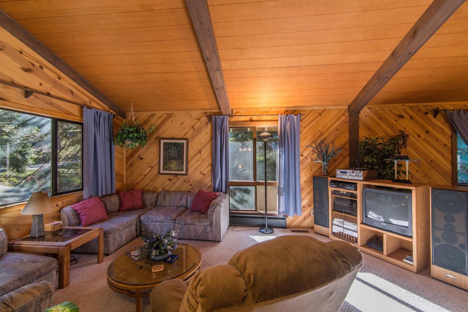 Ein gemütliches Blockhaus-Interieur mit Holzbalkendecke, einer Sofagarnitur, einem Couchtisch, einem Fernseher und einem Bücherregal.