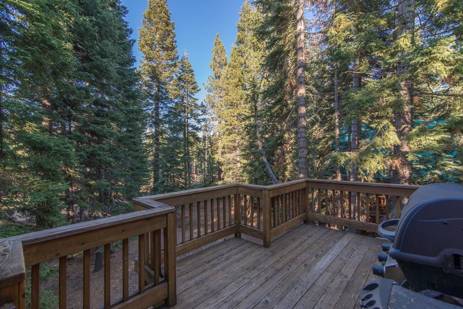 A wooden deck with a grill and a view of tall evergreen trees.