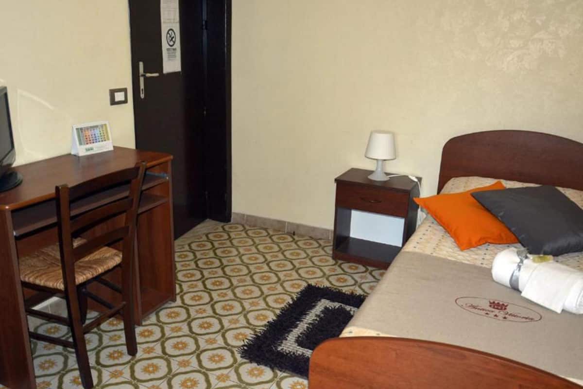 Une chambre d’hôtel comprenant un lit, un bureau avec une chaise, une table de chevet avec une lampe et un sol à motifs.