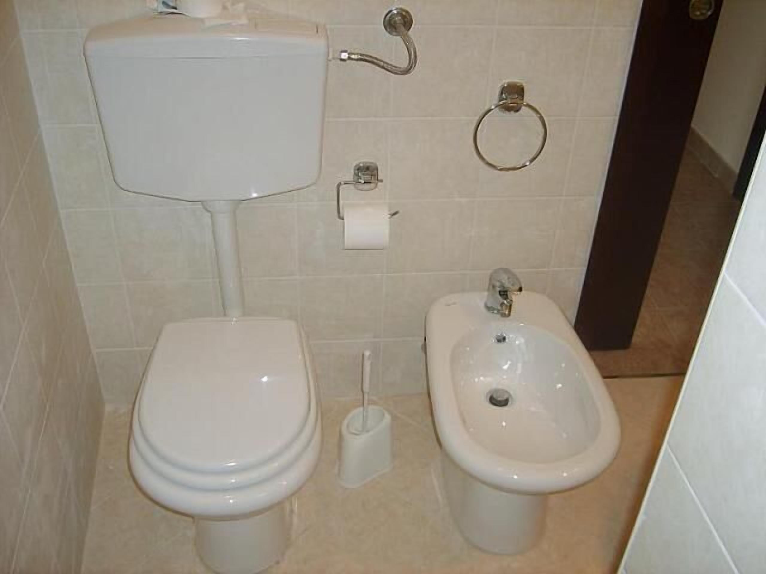 A bathroom with a toilet, bidet, and a toilet paper holder on the wall.