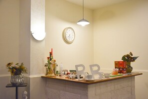 Een hotel receptie met een klok, een balie met diverse items, een vaas met bloemen en een hanglamp.