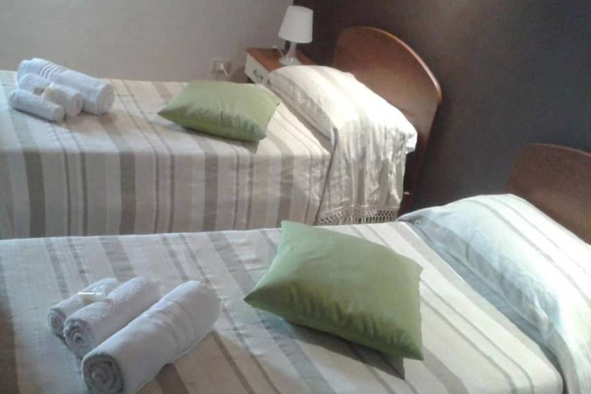 Deux lits simples avec une literie et des oreillers à rayures, une tête de lit en bois et une table de chevet avec une lampe.