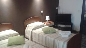 A hotel room with two beds, a TV, and a nightstand with a lamp.