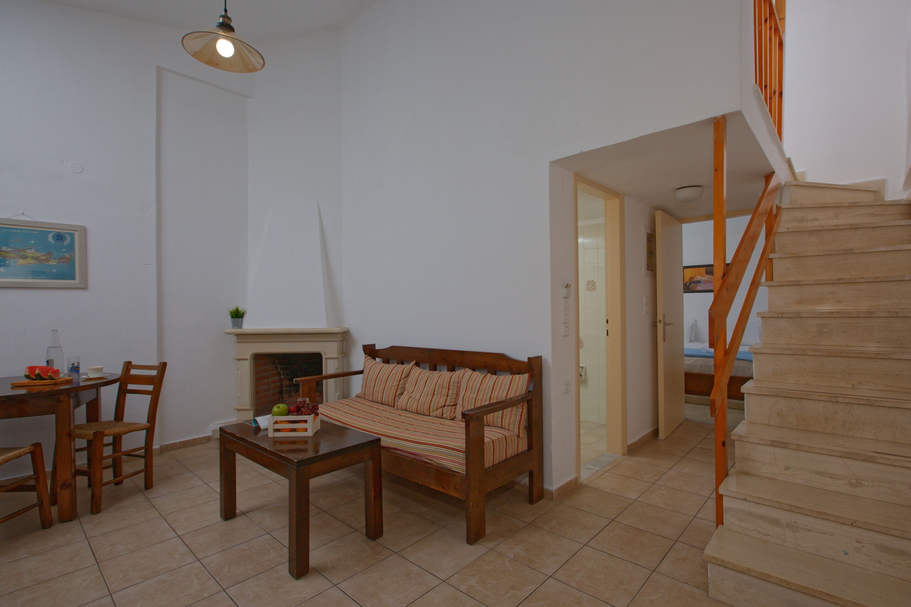 Una sala de estar con sofá, mesa de comedor, sillas, chimenea y escalera de madera.