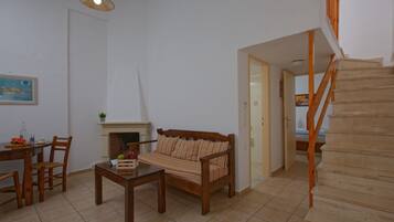 Una sala de estar con sofá, mesa de comedor, sillas, chimenea y escalera de madera.