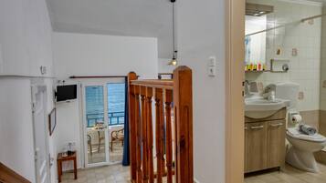 Baño con inodoro, lavabo y ducha. Una escalera de madera lleva a un balcón con vistas al mar.