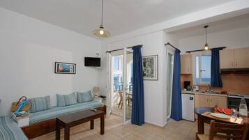 Un espacio habitable compacto con sofá, mesa de comedor, zona de cocina y balcón con cortinas azules.