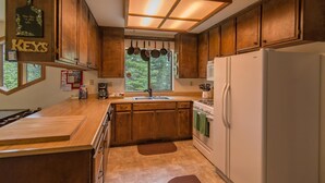 A kitchen with wooden cabinets, a white refrigerator, a stove, and a window with hanging pots. - Kelly 3 Bedroom Holiday Home By Tahoe Truckee (Truckee)