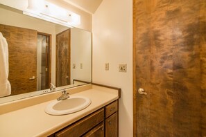 Ein Badezimmer mit Holztür, Waschbecken in Weiß, Spiegel und einer Leuchte darüber.