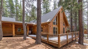 A cabin with a wooden deck and a covered porch, surrounded by tall pine trees. - Falcon Point 3 Bedroom Holiday Home By Tahoe Truckee (Truckee)