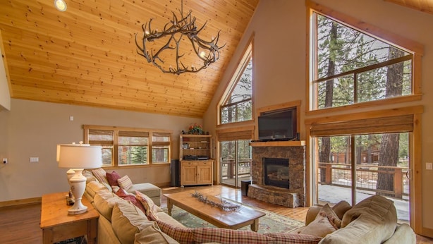 A spacious living room with a high ceiling, a stone fireplace, a large sofa, and a television. - Falcon Point 3 Bedroom Holiday Home By Tahoe Truckee (Truckee)