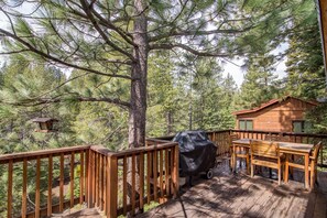 A wooden deck with a barbecue grill, wooden furniture, and a cabin in a forested area. - Serventi 3 Bedroom Holiday Home By Tahoe Truckee (Truckee)