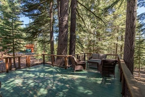 A wooden deck with wicker furniture, surrounded by tall trees. - Saunders 3 Bedroom Holiday Home By Tahoe Truckee (Truckee)