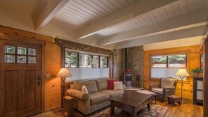 A cozy cabin interior with a wooden exterior, a stone fireplace, a sofa, a coffee table, and two lamps. - Saunders 3 Bedroom Holiday Home By Tahoe Truckee (Truckee)