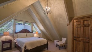 A bedroom with a large bed, two bedside tables with lamps, a wooden door, and a sloped ceiling with a chandelier. - Saunders 3 Bedroom Holiday Home By Tahoe Truckee (Truckee)