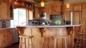 Eine Küche mit Holzschränken, einer Granitarbeitsplatte, einer Mikrowelle, einem Kühlschrank und zwei Barhocker.