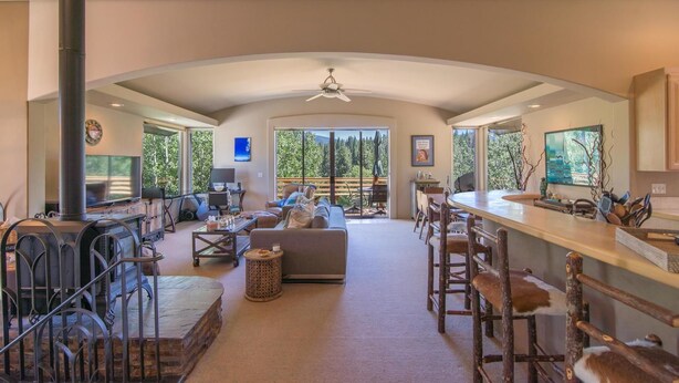 A spacious living area with a fireplace, seating, a kitchen bar, and large windows offering a view of the outdoors. - Palisades 4 Bedroom Holiday Home By Tahoe Truckee (Truckee)