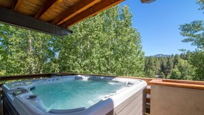 A hot tub on an outdoor deck with a wooden ceiling, surrounded by lush green trees and a clear blue sky. - Palisades 4 Bedroom Holiday Home By Tahoe Truckee (Truckee)