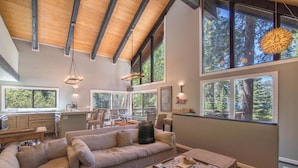 A spacious living area with a large sectional sofa, a dining table, and a kitchen area with a window overlooking a forest. - South Shore 5 Bedroom Holiday Home By Tahoe Truckee (Truckee)
