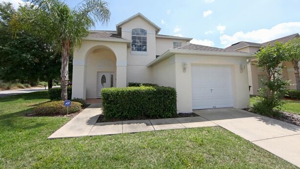 A single-story house with a garage, a front yard with a hedge, and a palm tree.