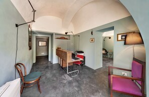A room with a desk, chairs, and a lamp. There are framed pictures on the wall and a ceiling light fixture. - Palazzo Melfi Suite - Hotel (Comiso)