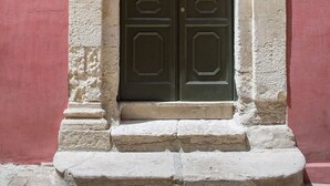 A double door with ornate metalwork and a stone frame, set in a building with a red wall and a stone base. - Palazzo Melfi Suite - Hotel (Comiso)