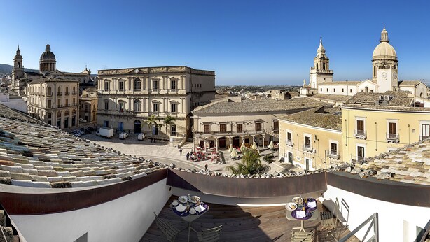 A rooftop terrace with tables and chairs, overlooking a historic cityscape with prominent buildings and a clear sky. - Palazzo Melfi Suite - Hotel (Comiso)