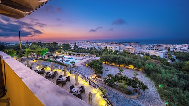 Una terraza con mesas al aire libre, piscina y vistas a la ciudad al atardecer.
