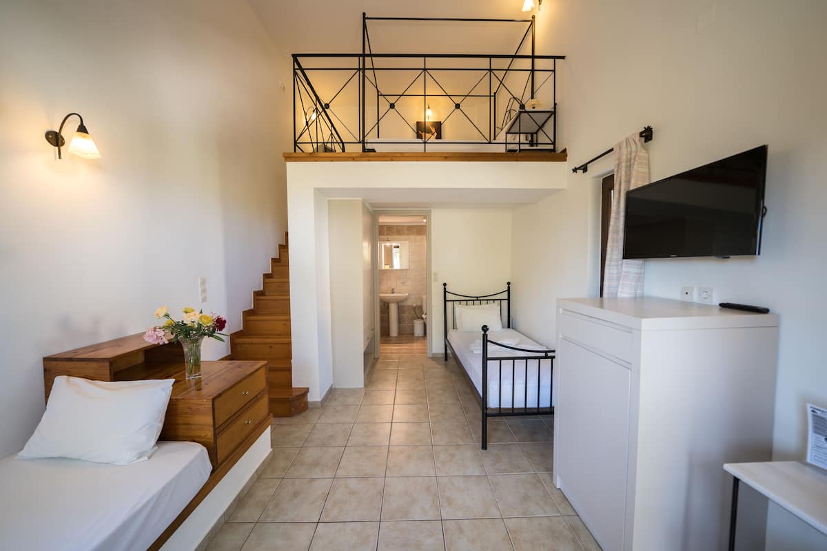 A modern bedroom with a wooden dresser, a bed, a nightstand, a TV, and a staircase leading to an upper level.