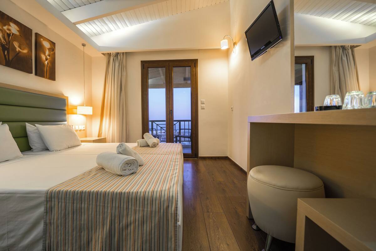 A hotel room with a bed, a desk, a chair, a TV, and a balcony with a view.