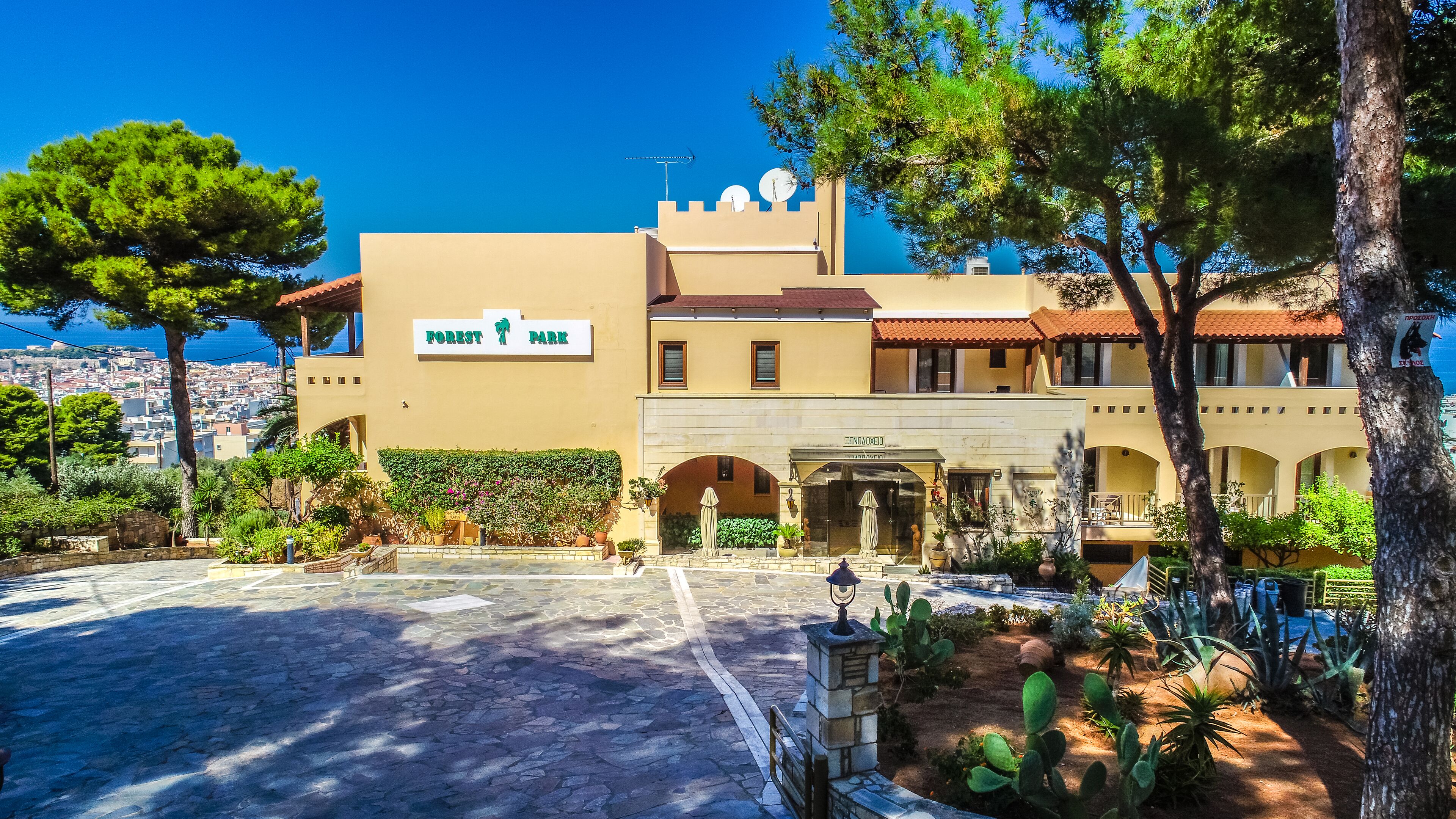 A hotel named Forest Park with a Mediterranean architectural style, featuring a courtyard with plants and a view of the city.