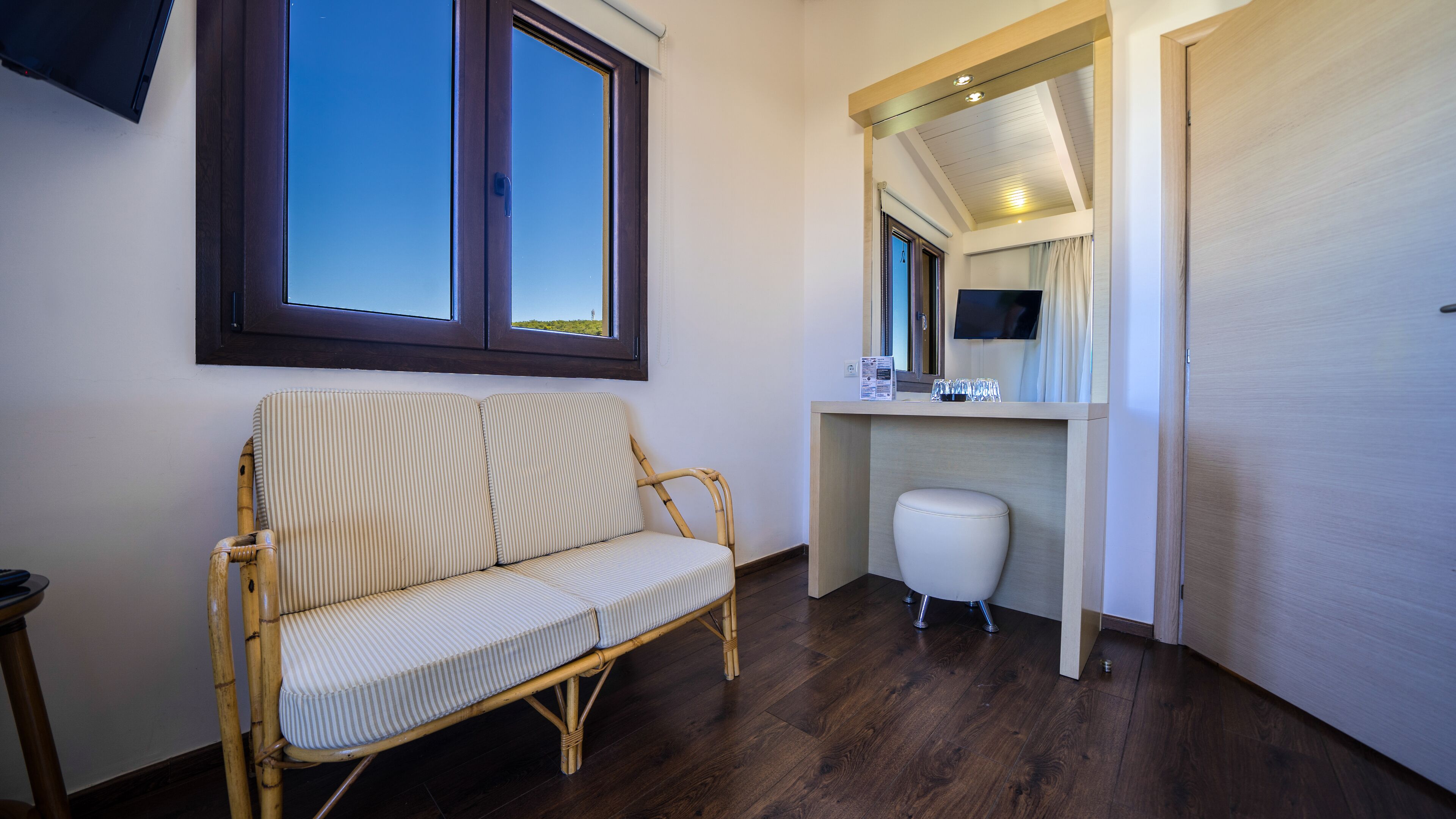 Ein Zimmer mit einem Korbssessel, einer kleinen weißen Toilette und einem Spiegel über einem Waschtisch mit Fernseher.