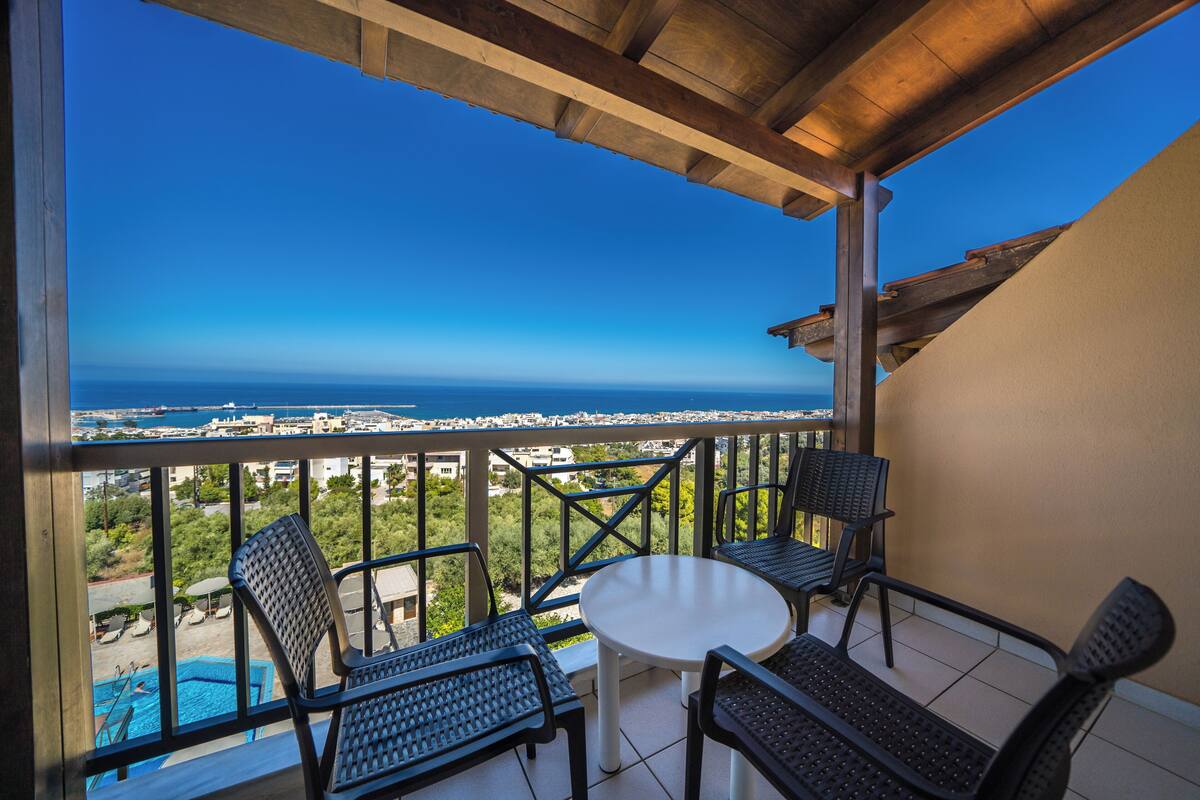 A balcony with a view of the sea, equipped with a table and four chairs.
