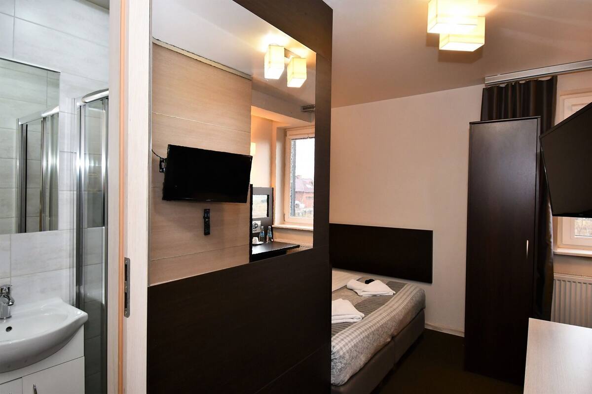 Una habitación de hotel compacta con cama, televisión, lavabo y espejo.