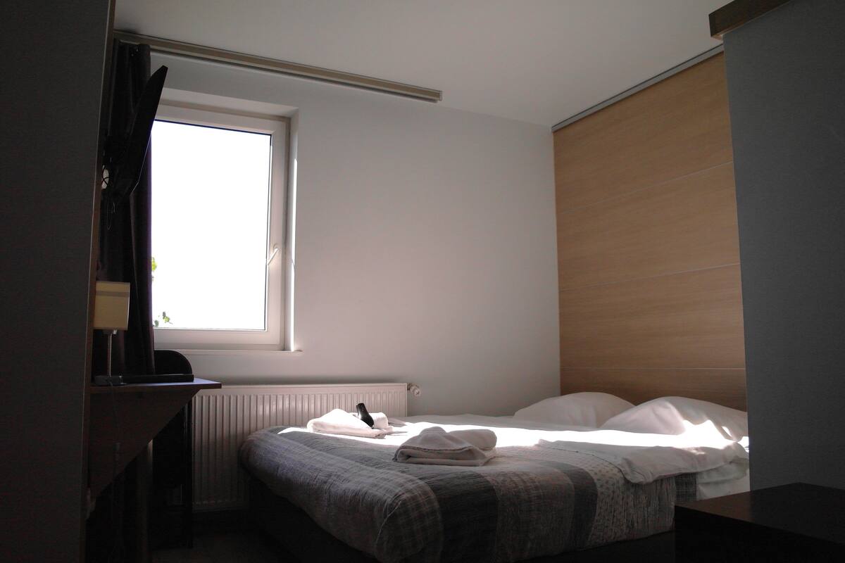 Un dormitorio con una cama, una ventana, un radiador y un escritorio con lámpara.