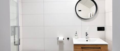 Une salle de bain moderne comprenant des toilettes, un lavabo avec un miroir et un espace douche.
