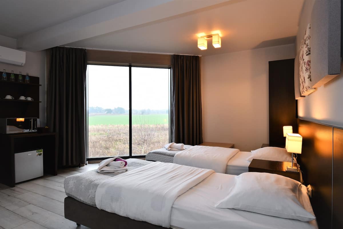 Habitación de hotel con dos camas, un escritorio con microondas, un refrigerador pequeño, una ventana grande con cortinas y un televisor montado en la pared.