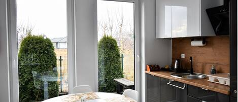 A modern kitchen with a round dining table, a sink, and cabinets. There are two windows providing a view of the outside.