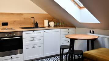 A kitchen with a skylight, a Bosch oven, white cabinets, a wooden countertop, and a round table with two stools.