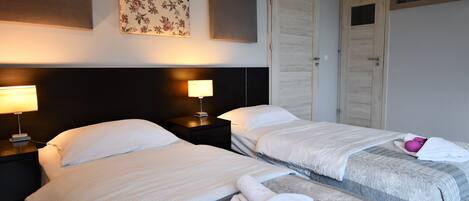 Habitación de hotel con dos camas, una mesita de noche con lámpara, una obra de arte floral en la pared y una puerta con ventanal.